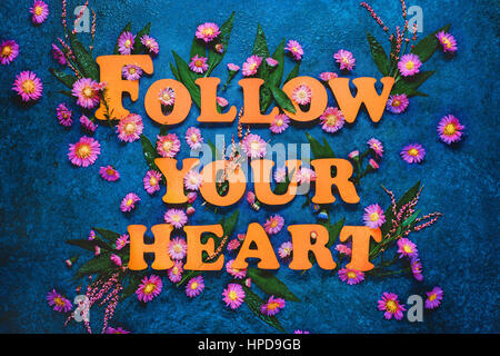 Folgen Sie Your Heart Schriftzug mit weißen und lila Blüten und Blätter auf einem dunklen Hintergrund Marmor. Buchstaben bestehen aus pastellfarbenen Papier. Stockfoto