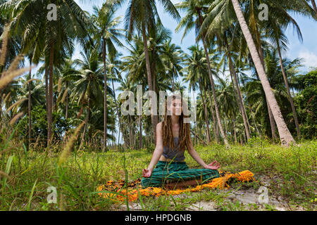 Junge Frau mit Dreadlocks machen Yoga unter Palmen sitzen Stockfoto