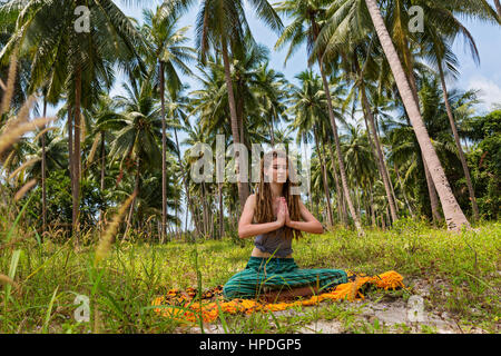 Junge Frau mit Dreadlocks machen Yoga unter Palmen sitzen Stockfoto