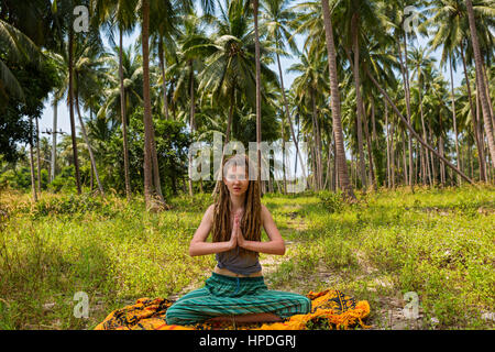 Junge Frau mit Dreadlocks machen Yoga unter Palmen sitzen Stockfoto