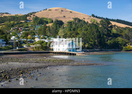 Akaroa, Canterbury, Neuseeland. Blick entlang der Küste der Hafen von Akaroa, auf der Sie bei Ebbe, Holz- Bootshaus im Vordergrund. Stockfoto