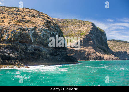 Akaroa, Canterbury, Neuseeland. Blick über das türkisfarbene Wasser des Pazifischen Ozeans zu den schroffen Klippen von Akaroa Kopf. Stockfoto