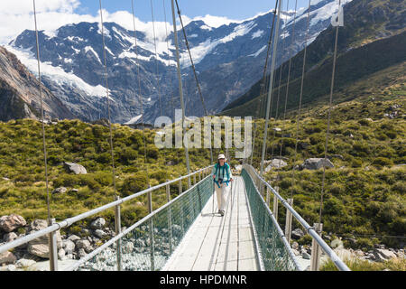 Aoraki/Mount Cook Nationalpark, Canterbury, Neuseeland. Wanderer auf der Hooker Valley Track Kreuzung Hängebrücke über den Hooker Fluss. Stockfoto