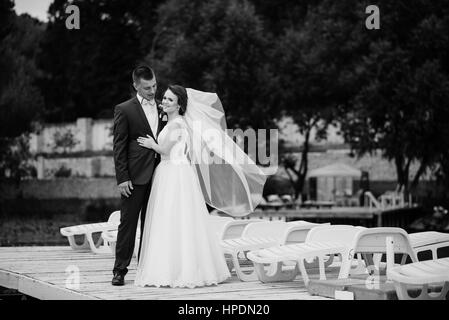 Charmante Hochzeitspaar umarmt am Pier des Docks. Schwarz / weiß Foto. Stockfoto