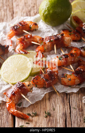 Tigergarnelen eingewickelt in Speck am Spieß mit Thymian und Kalk hautnah auf dem Tisch. vertikale Stockfoto