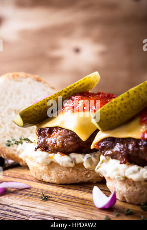 Hausgemachte Rindfleisch-Burger mit Gurken, Zahnstein und Tomaten Sauce serviert auf rustikalem Holzbrett Stockfoto