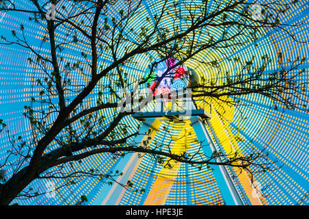 Silhouette der Äste vor Hintergrund der Bright Spinning Riesenrad im Frühjahr Abend oder Nacht. Bewegung verwischt Effekt rund um rotierende Illu Stockfoto