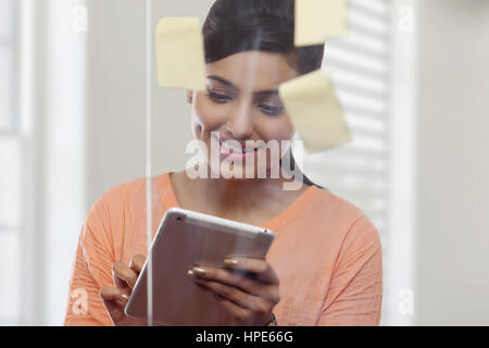 Frau hinter Glasscheibe mit Klebstoff Noten mit digital-Tablette in office Stockfoto