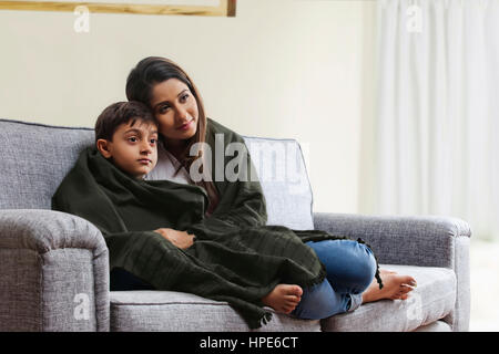 Mutter und Sohn, eingewickelt in eine Decke vor dem Fernseher im Wohnzimmer-sofa Stockfoto