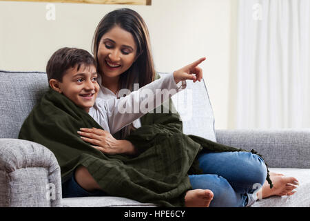 Lächelnde Mutter und Sohn in Fernsehen auf dem Sofa im Wohnzimmer Decke gehüllt Stockfoto