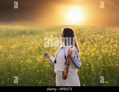 Junge Frau spielt Geige in einem Feld bei Sonnenuntergang Stockfoto