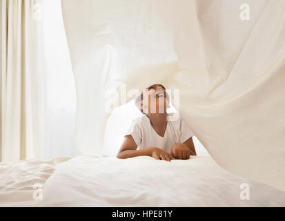 Kleiner Junge spielt unter weißen Bettlaken im Schlafzimmer Stockfoto