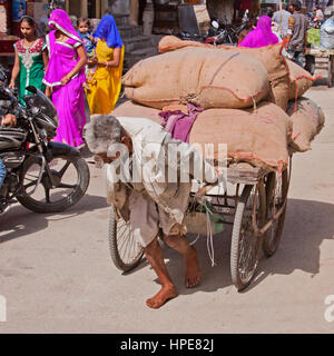 Ein unbekannter Mann zieht eine schwere Last durch die Straßen von Deogarh in Rajasthan. Träger werden häufig in der Region eingesetzt, um solche Lasten bewegen Stockfoto