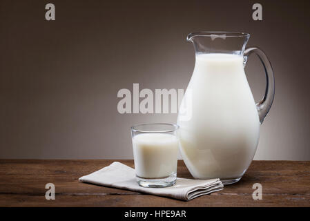 Glas und Krug voll Milch auf Holztisch Stockfoto