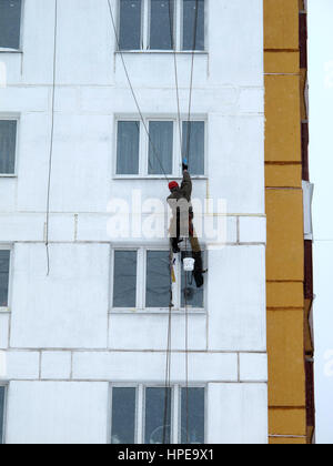 Industriekletterer in Helm und einheitliche Spachteln Wand auf Höhe. Riskante Aufgabe. Extreme Arbeit. Arbeitskraft Alpinist. Stockfoto