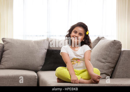 Lächelndes Mädchen sitzt im Schneidersitz auf sofa Stockfoto