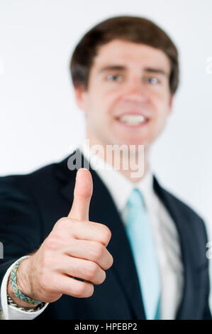 Kopf und Schulter Blick eines jungen Mannes zu dunklen Anzug den Daumen nach oben. Daumen im Fokus; Körper in den unscharfen Hintergrund. Stockfoto