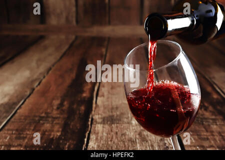 Rotwein wird aus Flasche, Glas auf hölzernen Hintergrund gegossen. Stockfoto