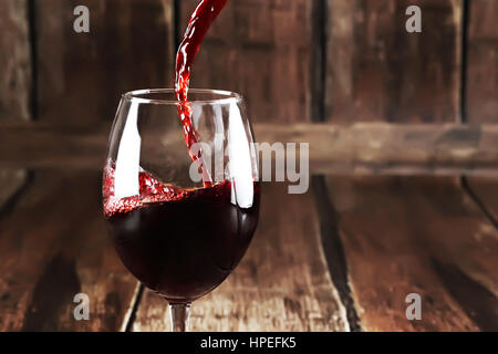 Rotwein wird aus Flasche, Glas auf hölzernen Hintergrund gegossen. Stockfoto