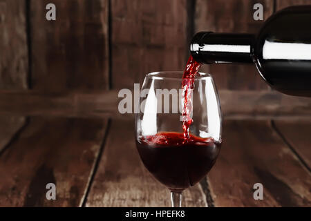 Rotwein wird auf hölzernen Hintergrund Glas gegossen. Stockfoto