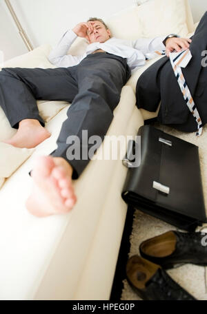 Modell veröffentlicht, Feierabend, Geschaeftsmann so Erschoepft Zuhause Auf der Couch - Ende des Arbeitstages, erschöpft Geschäftsmann nach der Arbeit zu Hause Stockfoto