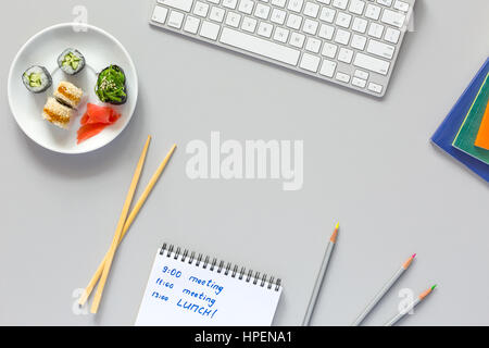 Ansicht von Office Arbeit Spitzenplatz auf grauen Tisch mit Computer-Bleistifte-Dokumente und Sushi Set mit hölzernen Stäbchen auf Tabelle Handschrift in eröffnet Notep Stockfoto