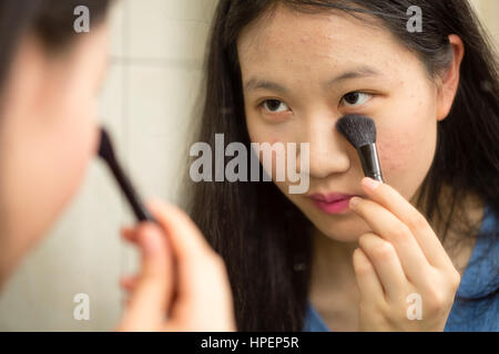 Chinesische Jugendliche setzen auf Make-up mit Pinsel vor Spiegel Stockfoto
