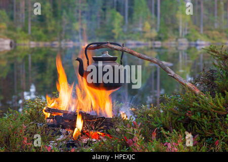 Geschwärzte Zinn Wasserkocher kochendes Wasser über Flammen von Lagerfeuer während der Wanderung entlang See Stockfoto