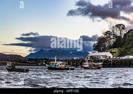 Cuillin Hills Mountain Range, über Loch Portree, auf der Isle Of Skye, Schottland, gegen einen dramatischen Himmel, hinter das Ende der Hafenpier und Boote Stockfoto