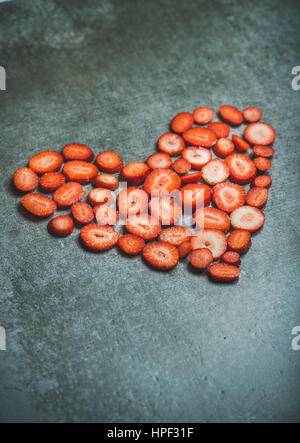 Stücke von frischen Erdbeeren in Form von Herzen auf grauem Beton Hintergrund, Tiefenschärfe, kopieren Sie Raum, vertikale Zusammensetzung. Valentinstag-Essen-co Stockfoto