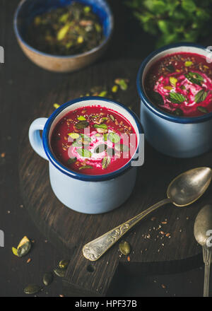 Frühling-Detox-rote Bete-Suppe mit Minze, Pistazien, Chia, Leinsamen, Kürbiskerne in blauer Emaille Becher in dunklem Holz. Saubere, gesunde Ernährung, Gemüse Stockfoto