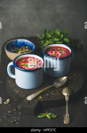 Rote-Bete-Suppe mit Minze, Pistazien, Chia, Leinsamen, Kürbiskerne in blauer Emaille Becher in dunklem Holz, Textfreiraum Frühling. Sauber, Essen, Gesundheit Stockfoto