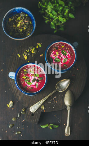 Rote-Bete-Suppe mit Minze, Pistazien, Chia, Leinsamen, Kürbiskerne in blauer Emaille Becher in dunklem Holz, Ansicht von oben im Frühjahr. Saubere, gesunde Ernährung, Stockfoto