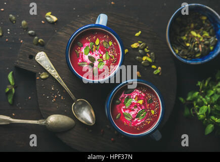 Frühling-Detox-rote Bete-Suppe mit Minze, Pistazie, Chia, Flachs und Kürbis Samen in blauer Emaille Becher in dunklem Holz, Ansicht von oben. Sauber, Essen, Stockfoto