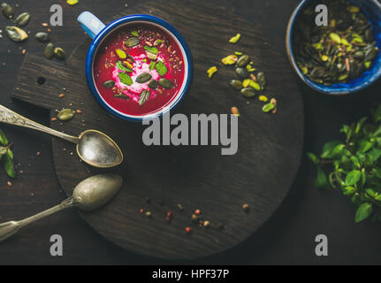 Frühling-rote Bete-Suppe mit Minze, Pistazien, Chia, Leinsamen, Kürbiskerne in blauer Emaille Becher in dunklem Holz, Draufsicht, Textfreiraum. Reinigen, eatin Stockfoto