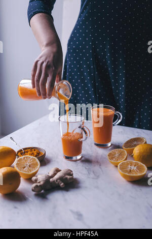 Frau Orange, Zitrone und Karotten-Saft mit Kurkuma und Ingwer in ein Glas gießen Stockfoto