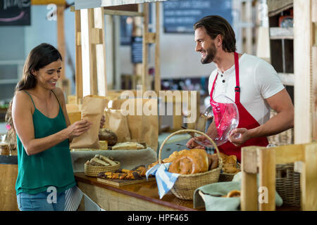 Lächelnde Kundin erhalten ein Paket von Bäckerei Personal am Schalter in der Backstube Stockfoto