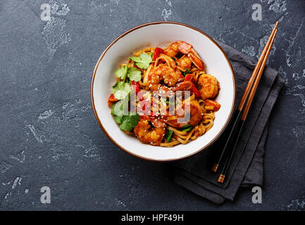 Stir-Fry Udon-Nudeln mit Garnelen in Schale und Stäbchen auf dunklem Stein Textfreiraum Stockfoto