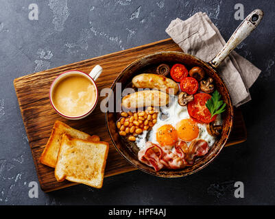 Englisches Frühstück in Pfanne mit Spiegelei, Würstchen, Speck, Bohnen, Toast und Kaffee auf dunklen Stein Hintergrund Stockfoto