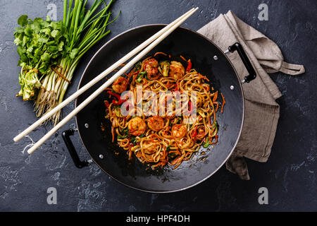 Stir-Fry Udon-Nudeln mit Garnelen in Wok-Pfanne auf dunklen Stein Hintergrund Stockfoto