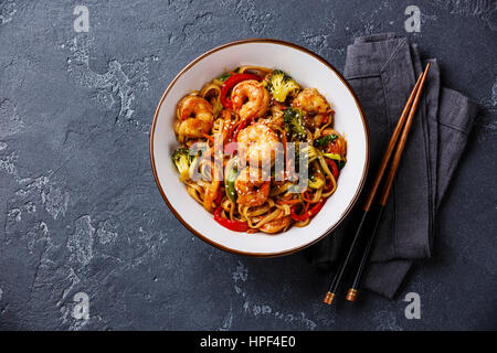 Stir-Fry Udon-Nudeln mit Garnelen in Schale und Stäbchen auf dunklem Stein Textfreiraum Stockfoto