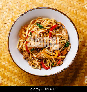 Udon Nudeln mit Hühnerfleisch und Sesam in Schüssel mit Bambus Tablett Hintergrund Nahaufnahme Wokken Stockfoto