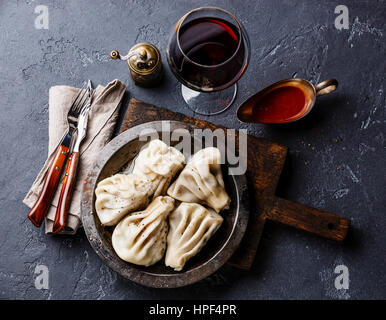 Georgische Teigtaschen Khinkali mit Fleisch, Tomaten pikante Sauce Satsebeli und Wein auf dunklen Stein Hintergrund Stockfoto