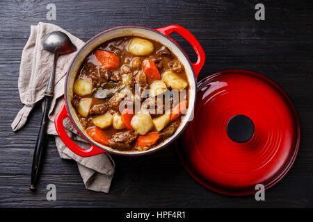 Rind Fleisch-Schmortopf mit Kartoffeln, Möhren und Gewürzen in gusseisernen Pfanne auf verbrannte schwarze Holz Hintergrund Stockfoto