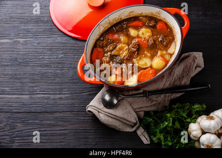 Rind-Fleisch-Eintopf mit Kartoffeln, Möhren und Gewürzen in Gusseisen Topf auf verbranntes Holz schwarzem Textfreiraum Stockfoto