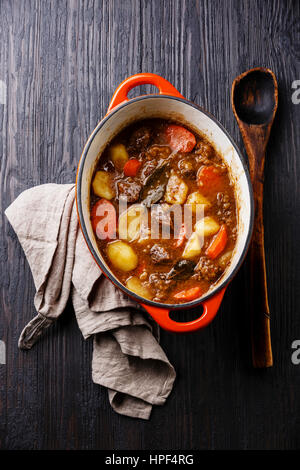 Rind-Fleisch-Eintopf mit Kartoffeln, Möhren und Gewürzen in Gusseisen Topf auf verbrannte schwarze Holz Hintergrund Stockfoto