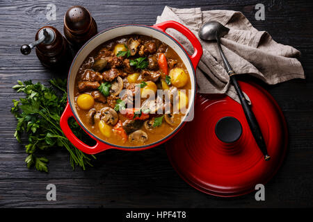 Rindfleisch geschmort mit Kartoffeln, Möhren und Gewürzen in gusseisernen Pfanne auf verbrannte schwarze Holz Hintergrund Stockfoto