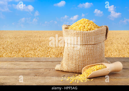 Bulgur oder Couscous im Sack. Bulgur in Tasche am Tisch mit Weizenfeld auf dem Hintergrund. Landwirtschaft und Ernte-Konzept. Goldene Weizenfeld Stockfoto