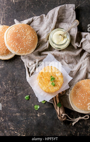 Zutaten für die Herstellung von veganen Burger. Veggie-Käse und Zwiebel Schnitzel, Joghurt-Sauce, Hamburgerbrötchen und Kräutern, serviert auf Holzbrett mit Textil auf d Stockfoto