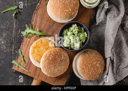 Zutaten für die Herstellung von veganen Burger. Veggie-Käse und Zwiebel-Koteletts, Joghurt-Sauce, Hamburger-Brötchen, Kräuter und Avocado-Salat, serviert auf hölzernen WLAN an Bord Stockfoto